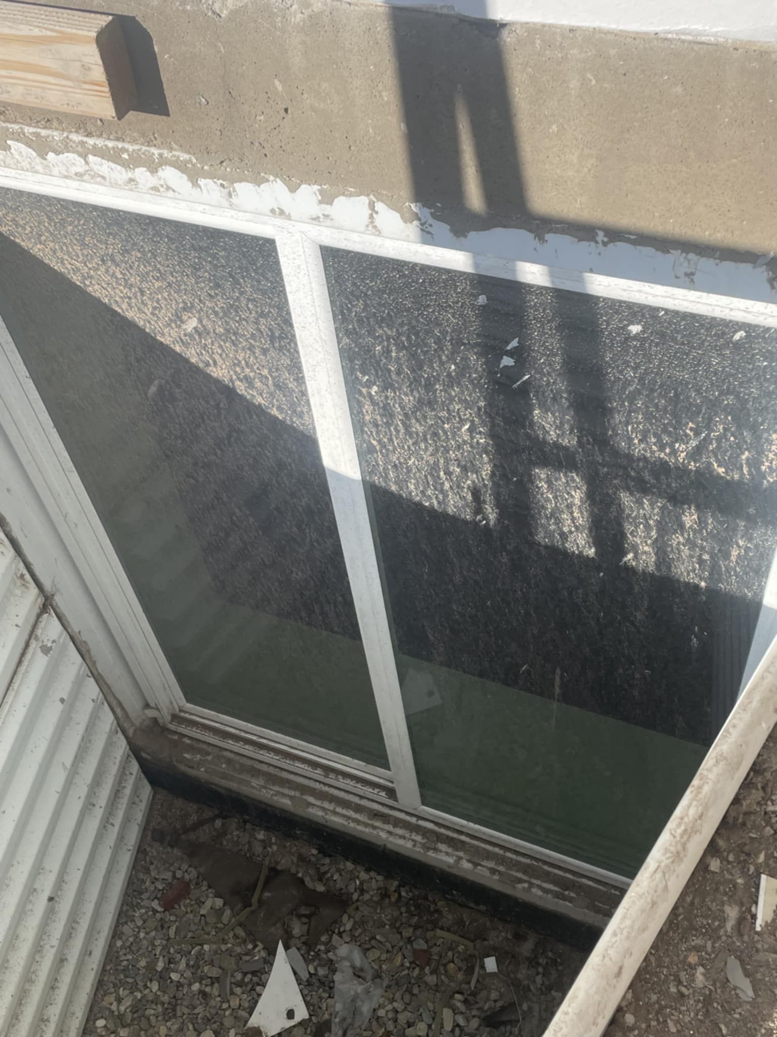 A window in a concrete and corrugated metal structure. The glass is dirty, showing sunlight and shadows.