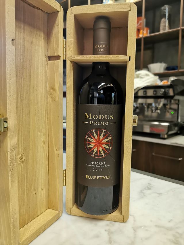 Mano che regge una bottiglia di vino blu scuro con l'etichetta