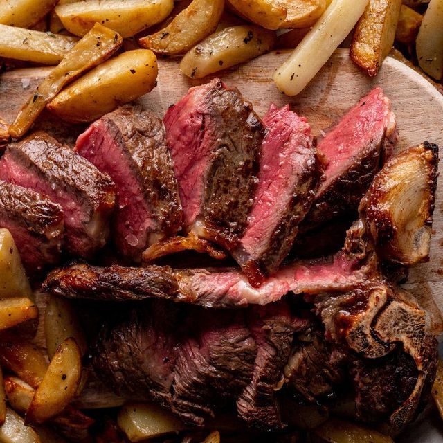 Macellaio che taglia la carne cruda con un grosso coltello su un tagliere bianco.