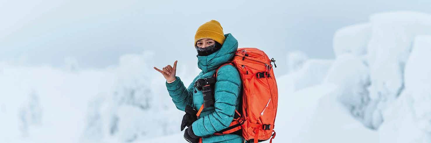 Eine Person mit einem orangefarbenen Rucksack steht im Schnee.