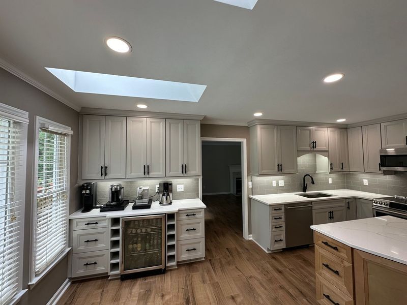 Modern kitchen with light gray cabinets, white countertops, and wooden floors. 