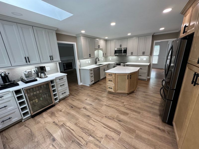 Modern kitchen with light wood floor, gray cabinets, black appliances, and a central island.
