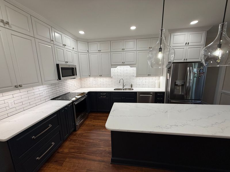 Modern kitchen with white and dark blue cabinets, stainless steel appliances, and white countertops.