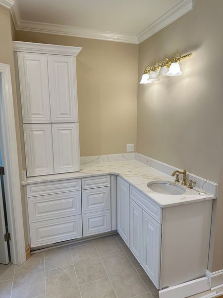White bathroom cabinetry with a countertop, sink, and light fixture against a beige wall.