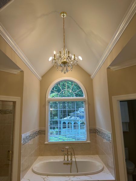 Bathroom with a bathtub, arched window, and a crystal chandelier. 
