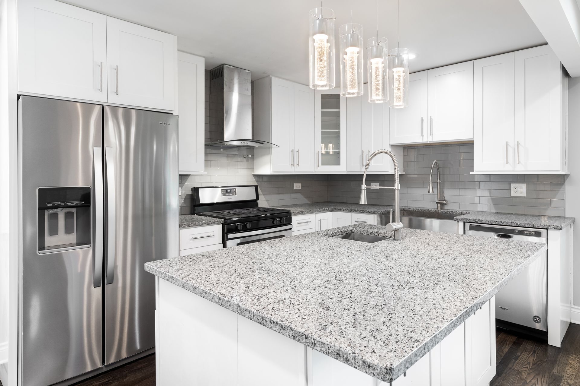 Modern white kitchen with stainless steel appliances, granite island, and pendant lights.