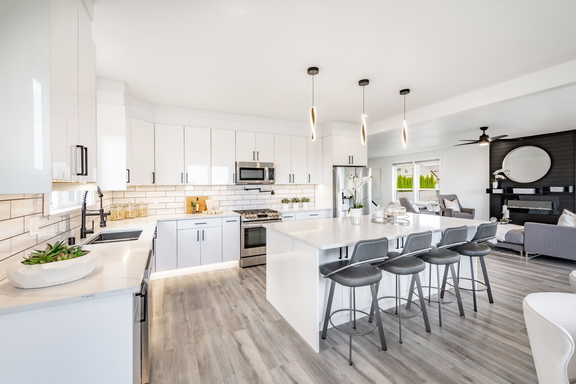 Modern white kitchen with island seating, opening to a living area with fireplace and outdoor access.