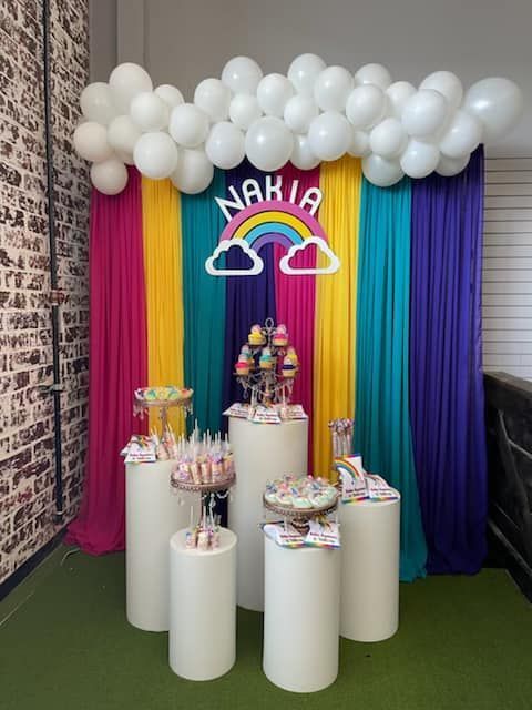 Rainbow-themed party backdrop with white cloud balloons
