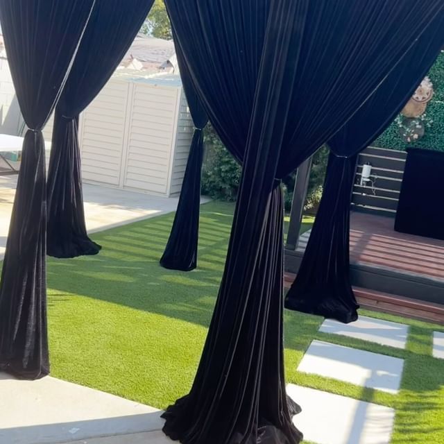 Black draped fabric hangs from a pergola on green turf