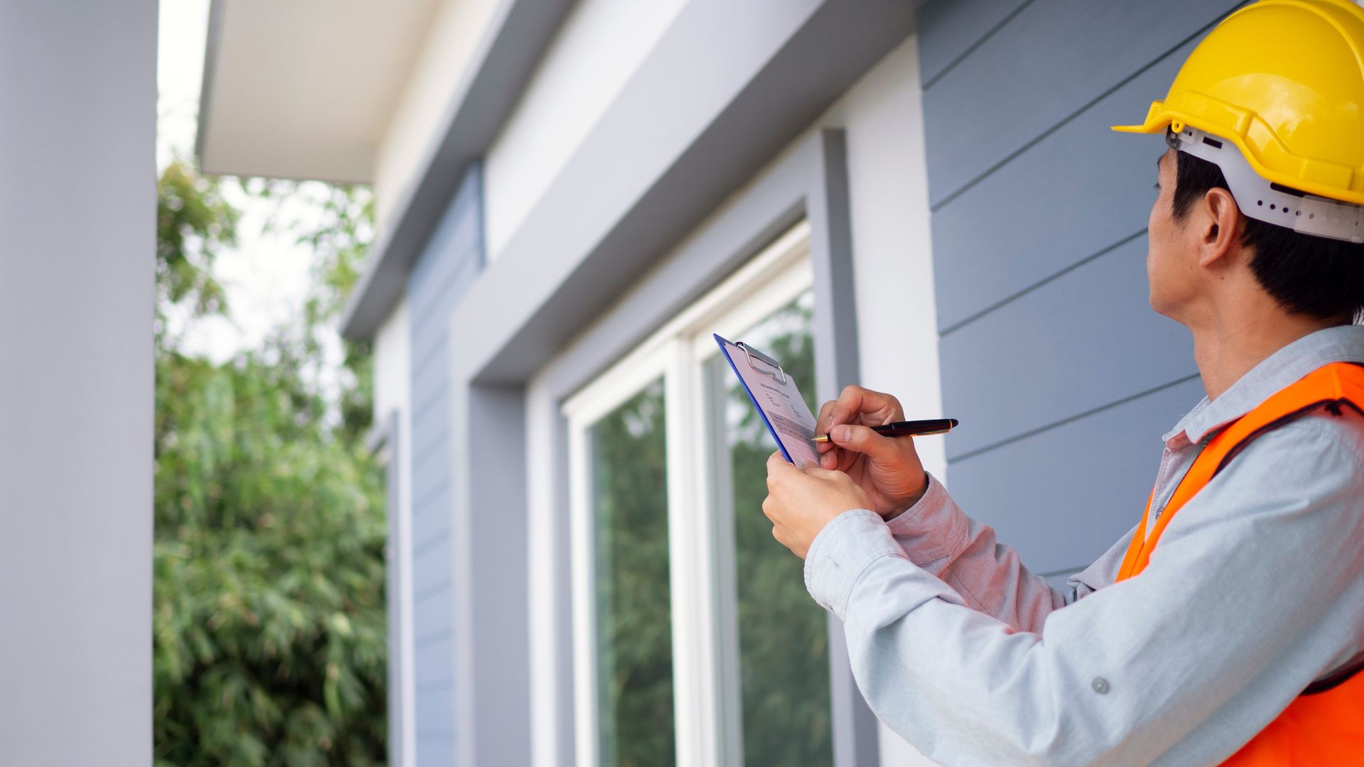 Home inspector wearing safety vest writing notes on clipboard inspecting house windows. Home inspector wearing safety vest writing notes on clipboard inspecting house windows.