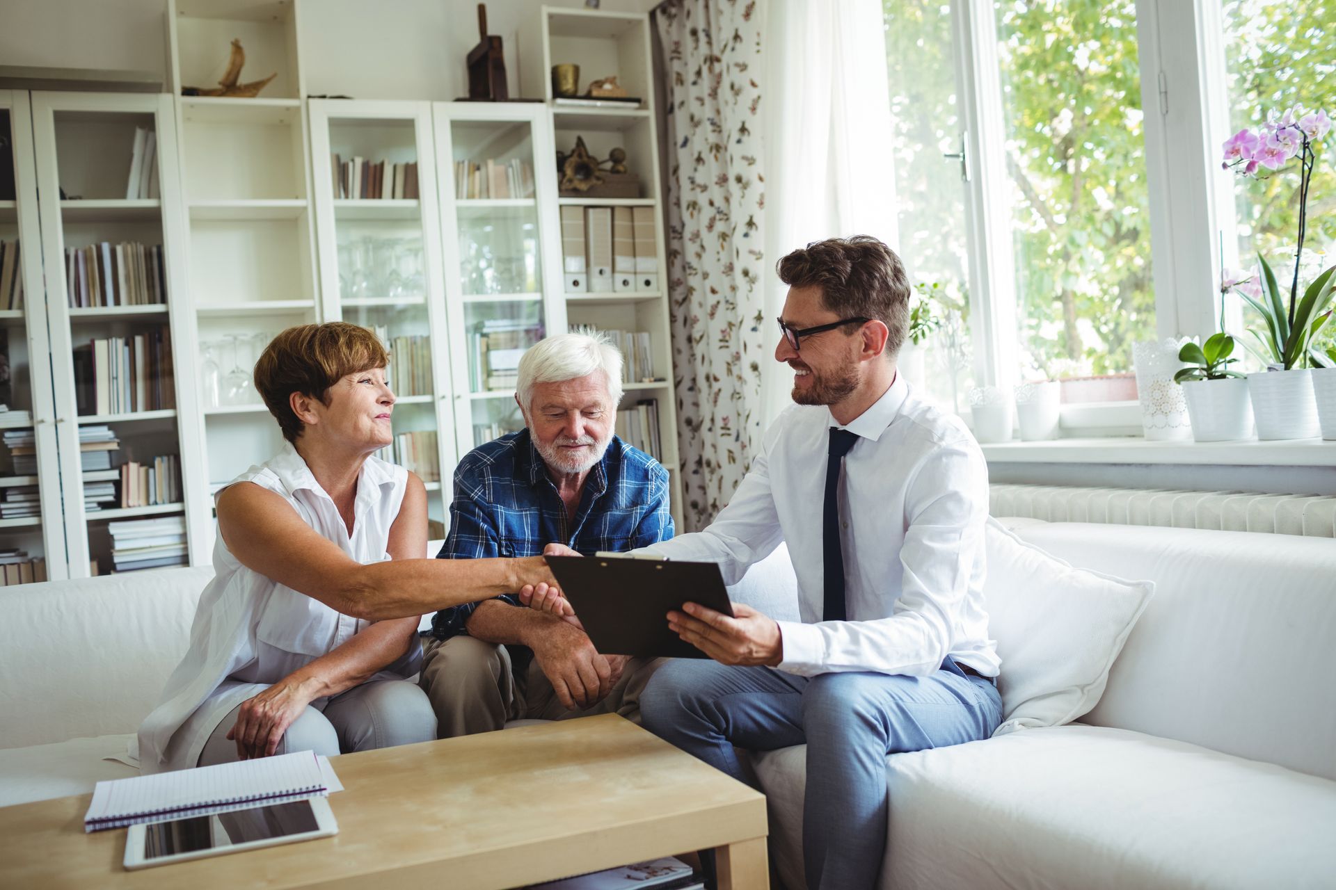 Three people discussing a document on a couch in a bright living room with a laptop on the table. Three people discussing a document on a couch in a bright living room with a laptop on the table.