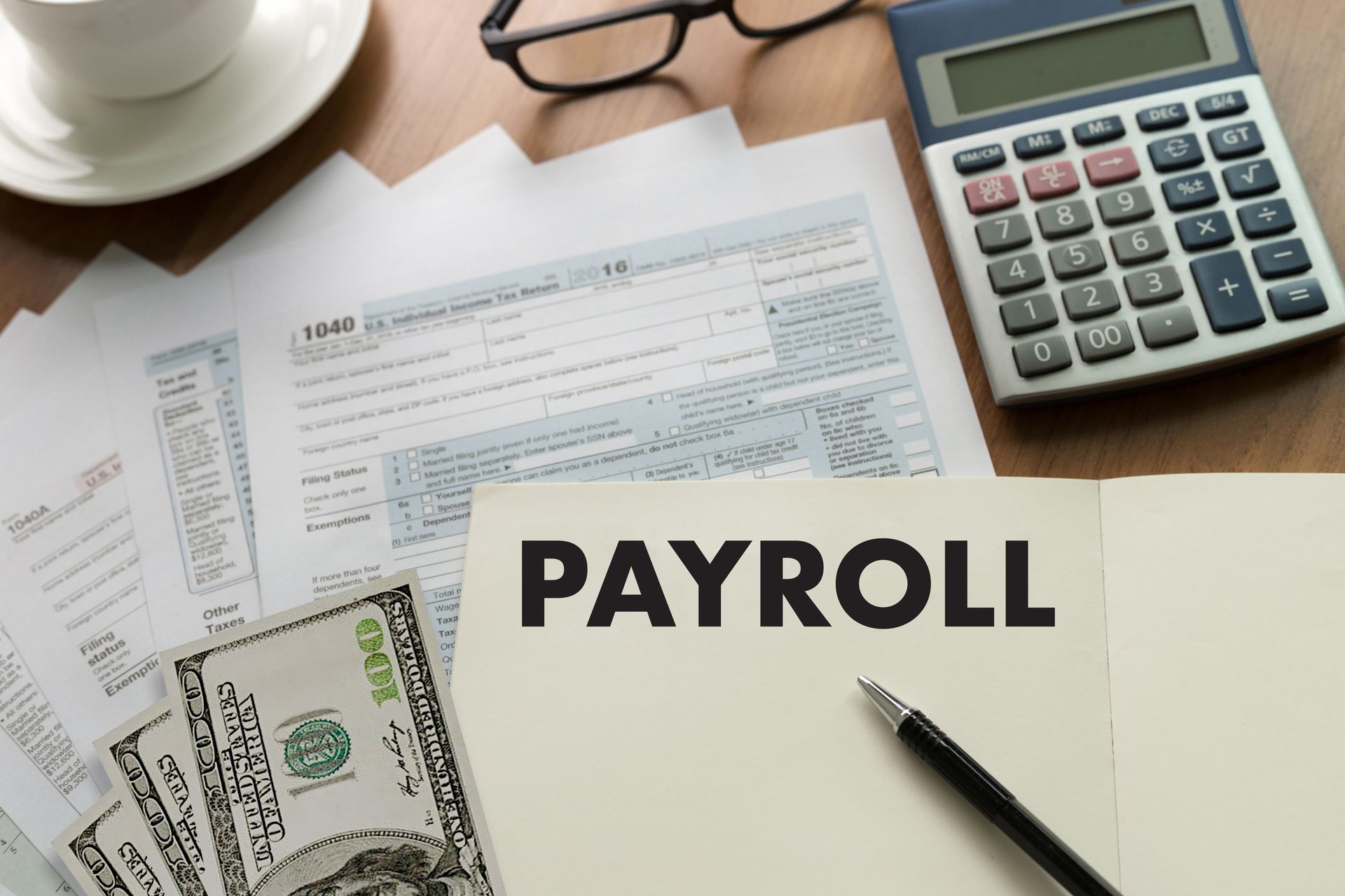Payroll documents, calculator, cash, and pen on a desk with a coffee cup Payroll documents, calculator, cash, and pen on a desk with a coffee cup