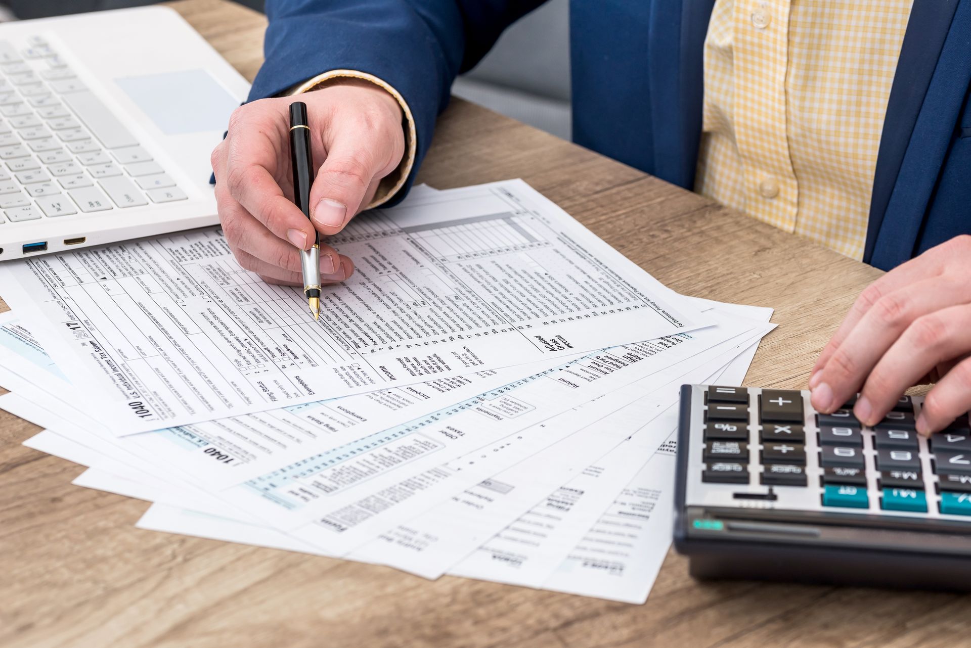 Two people reviewing financial forms at a desk, one writing and one using a calculator. Two people reviewing financial forms at a desk, one writing and one using a calculator.