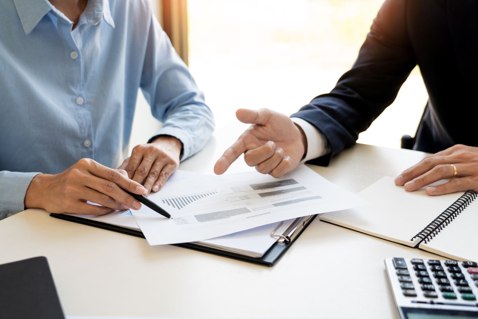 Two people reviewing documents and pointing at paperwork during a meeting at a desk Two people reviewing documents and pointing at paperwork during a meeting at a desk