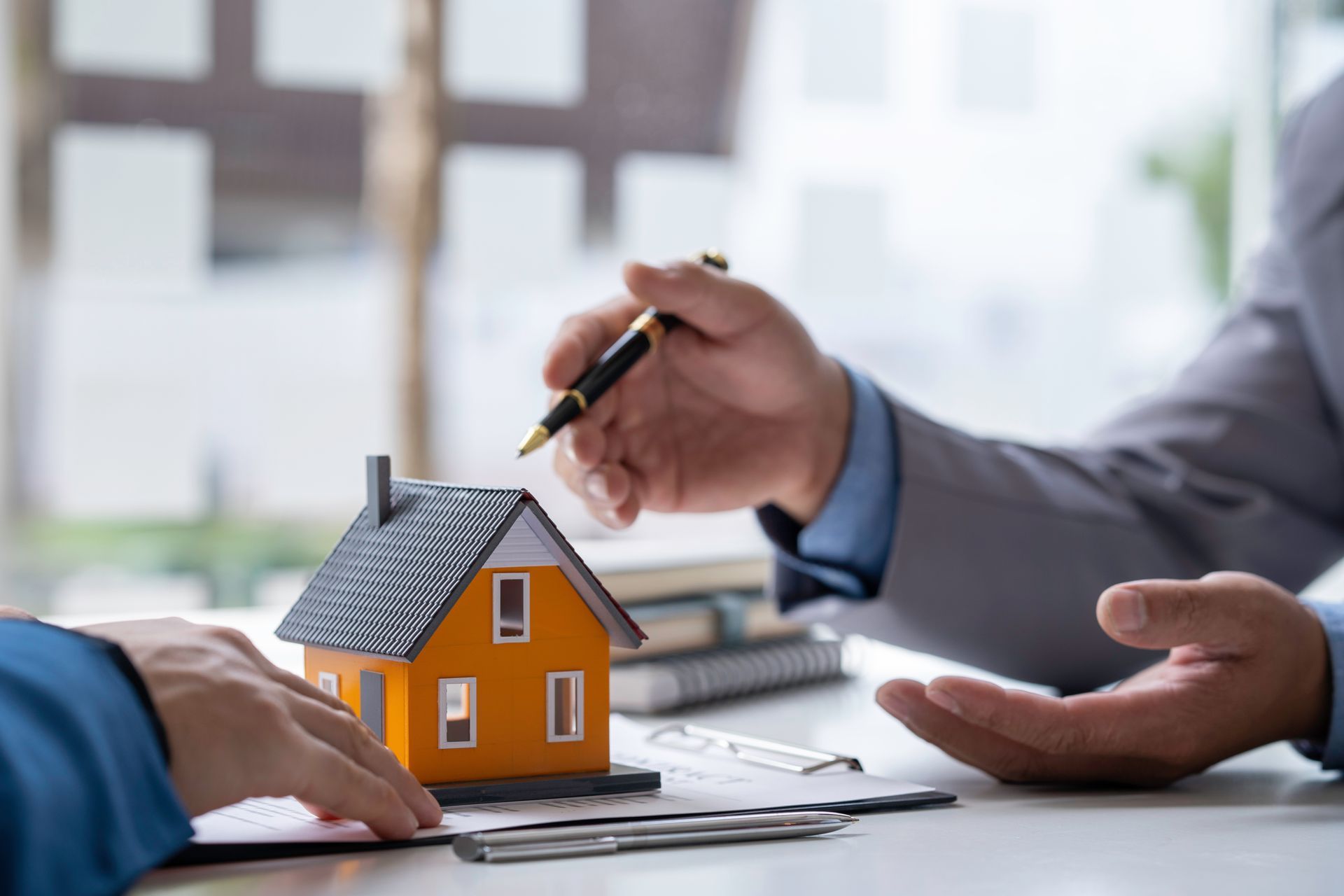 Hands presenting a small house model during a real estate consultation