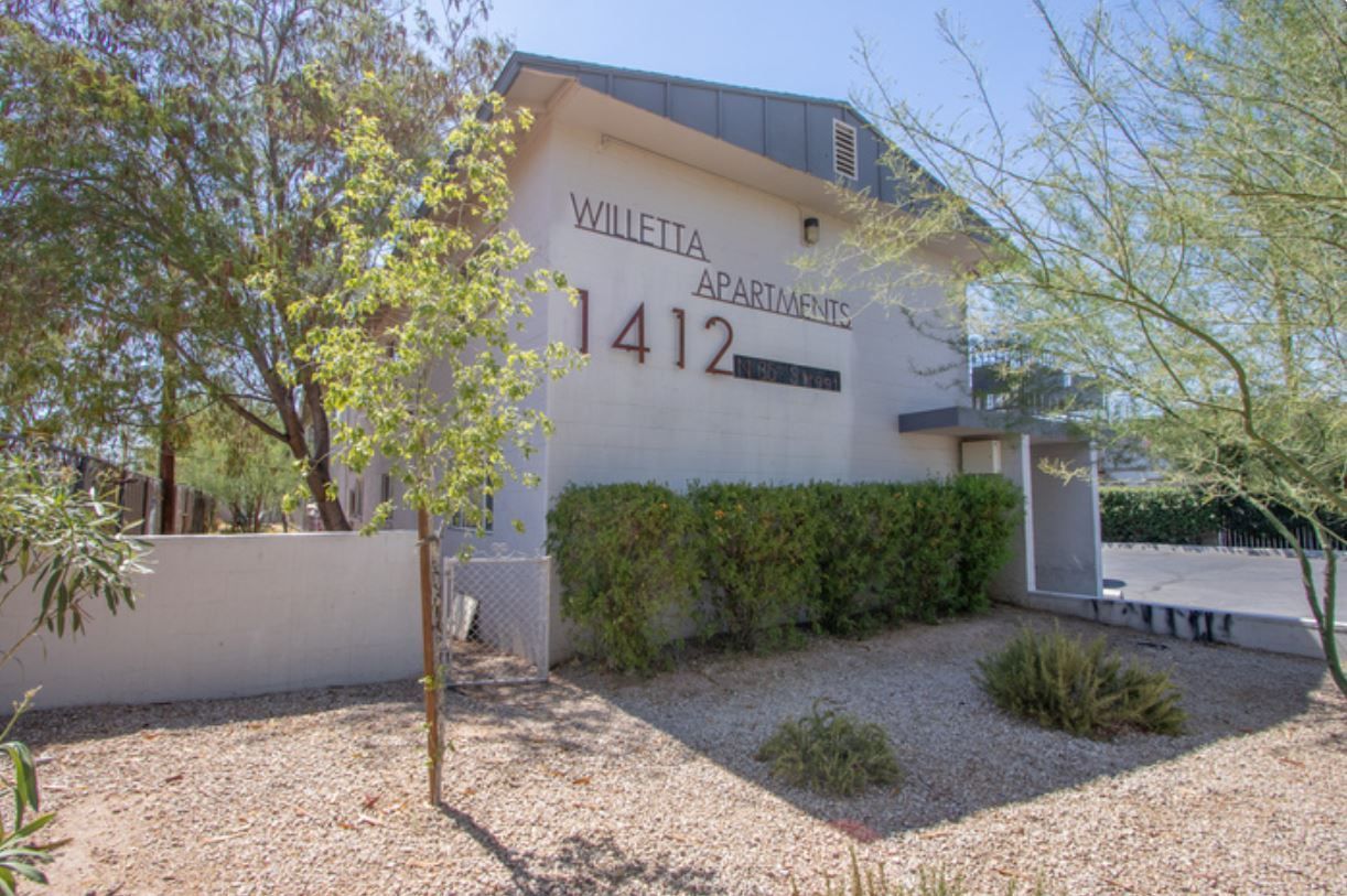 White exterior of the Huerta Apartments, address 1412, with tan gravel and green bushes.