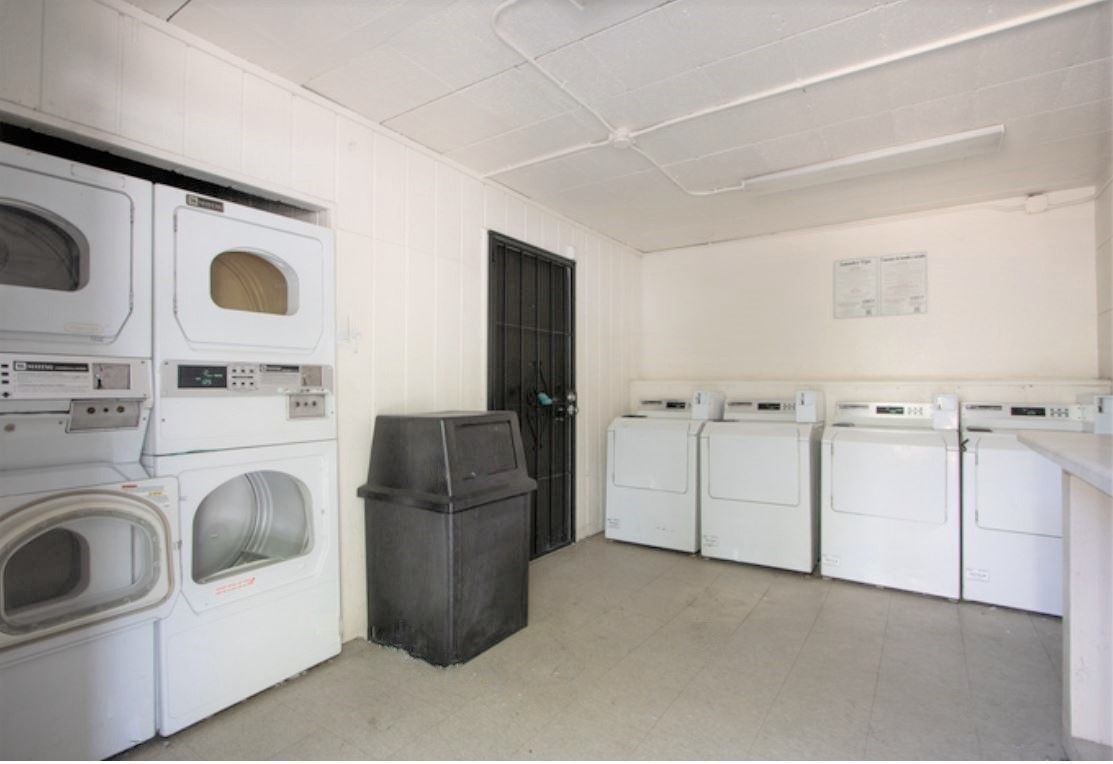 Laundry room with white appliances, black trash can, and a closed black door.