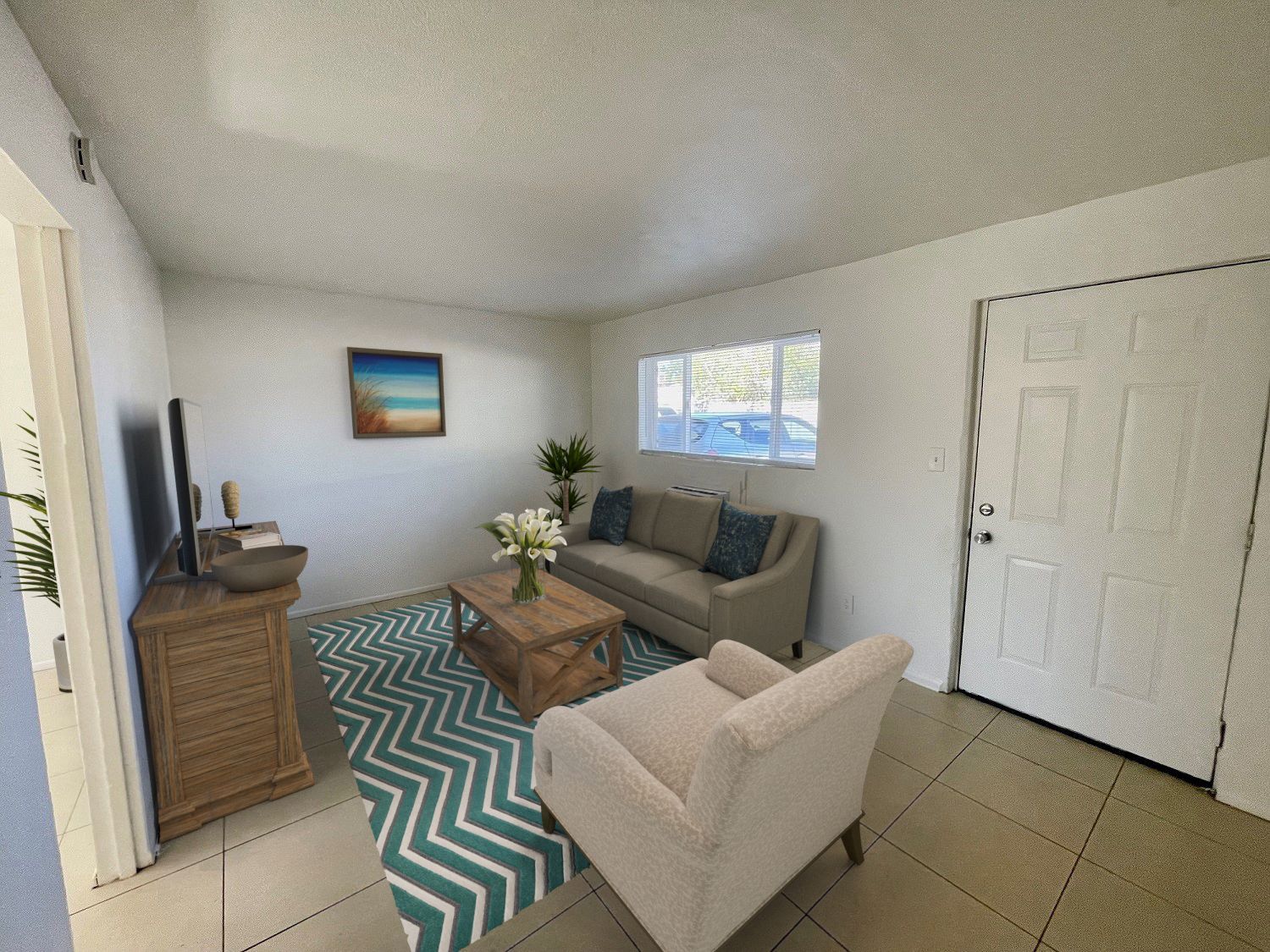 Living room with sofa, armchair, rug, and coffee table. White walls, wood cabinet, artwork, and door.