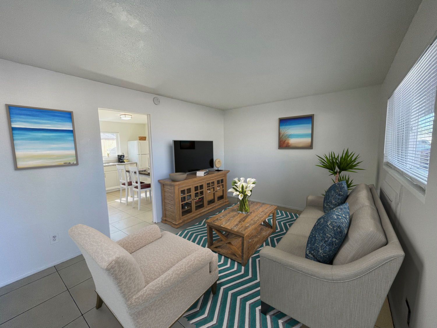 Living room with neutral furniture, ocean art, TV, and patterned rug.