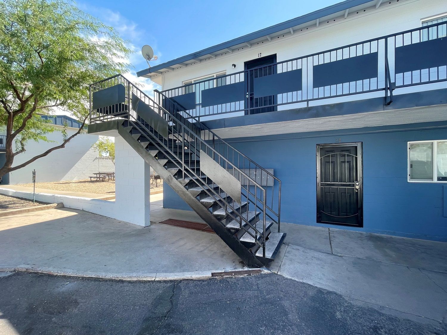 Exterior of a two-story apartment building with metal staircase. Blue and white facade with black doors and railing.