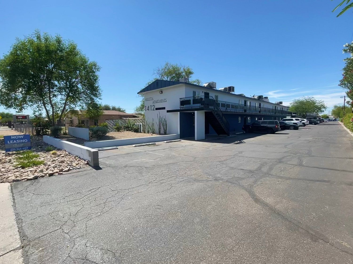 Apartment building with blue trim and a small parking area, on a sunny day.