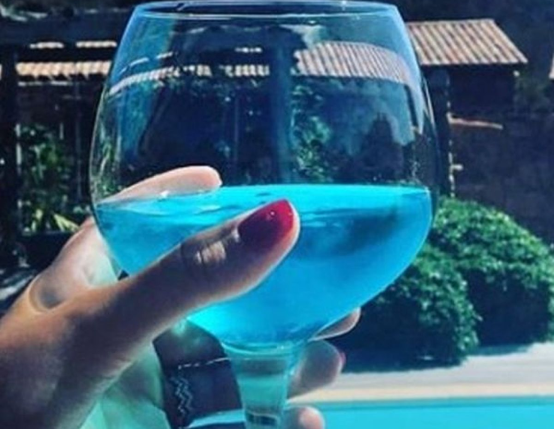 A person holding a glass of blue liquid in front of a pool