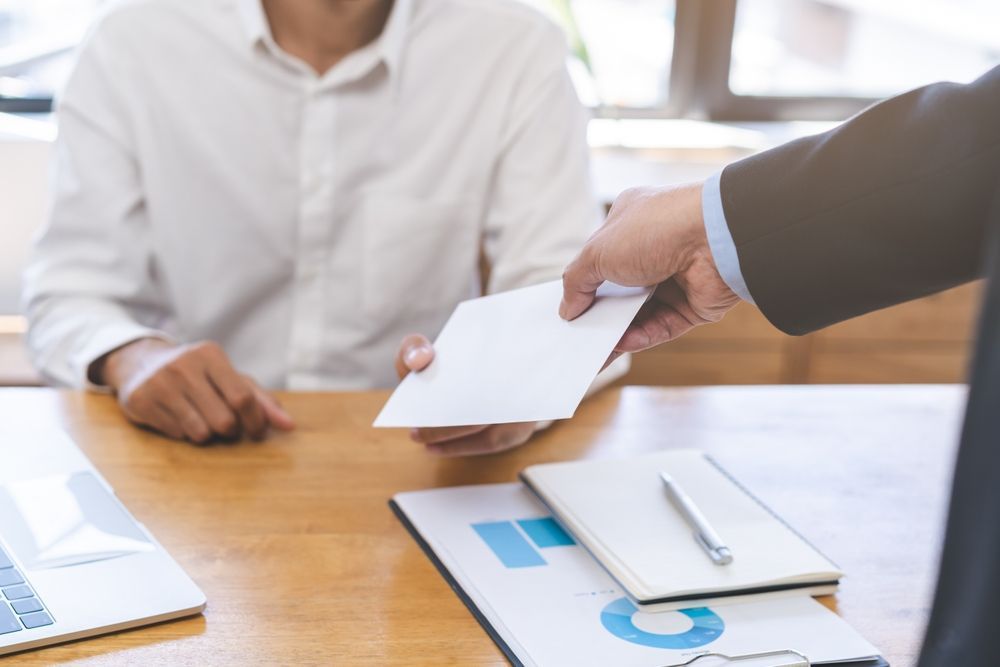 A man is giving an envelope to another man at a desk.
