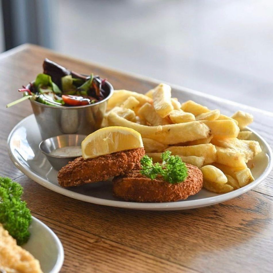 A plate of food with fried fish and french fries on a wooden table.