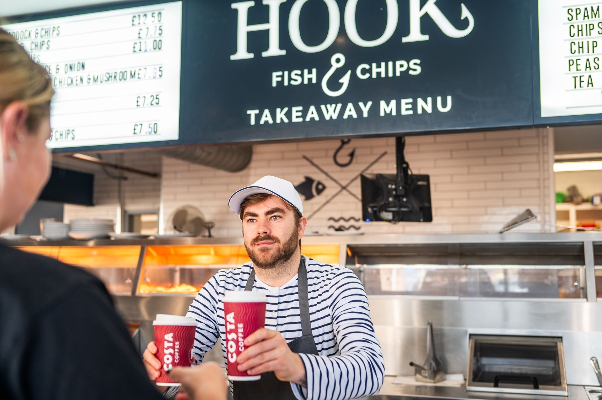 A man is serving a woman at a hook fish and chips takeaway menu.
