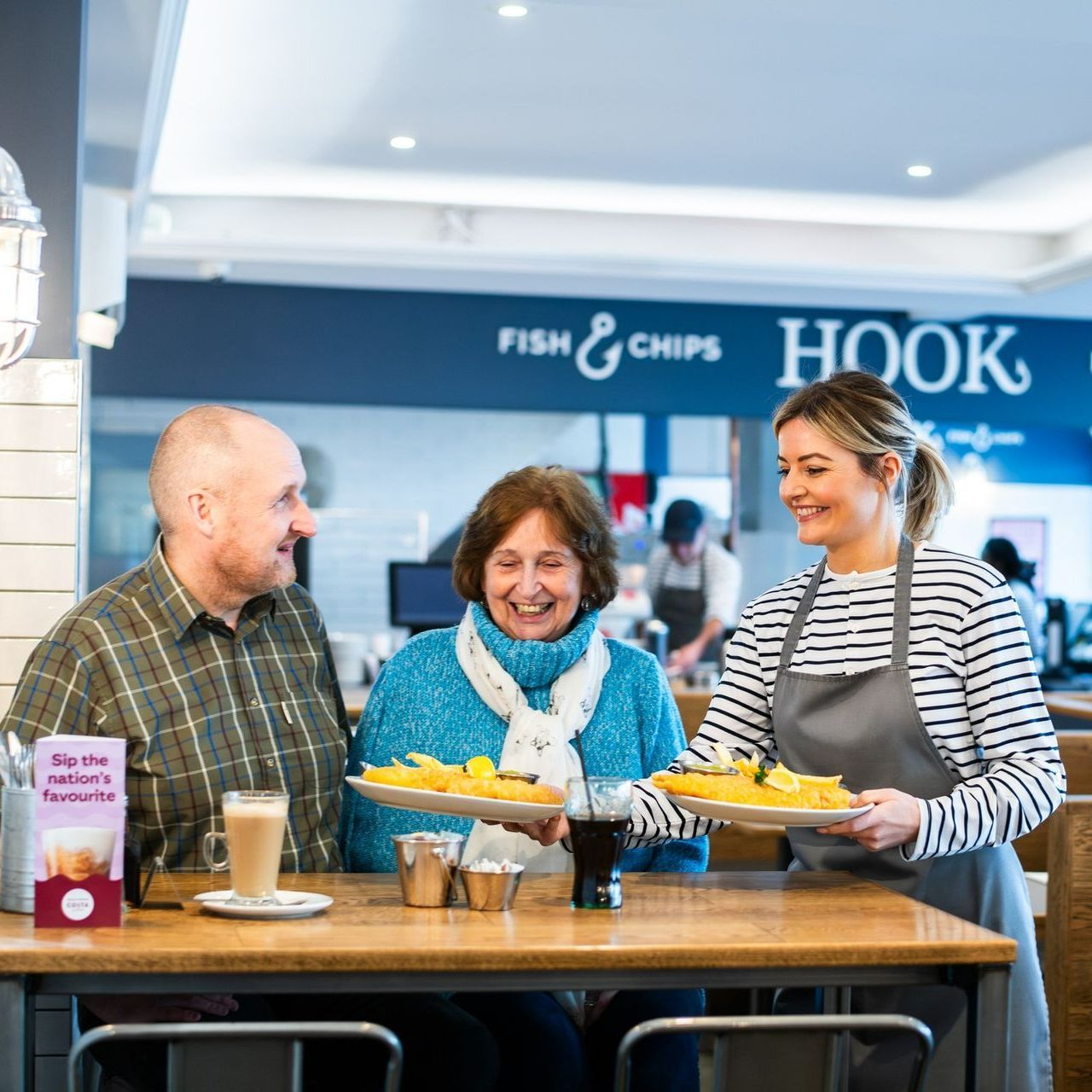 A group of people are sitting at a table in a restaurant holding plates of food.