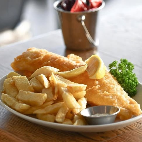 A plate of fish and chips with a bucket of tomatoes in the background