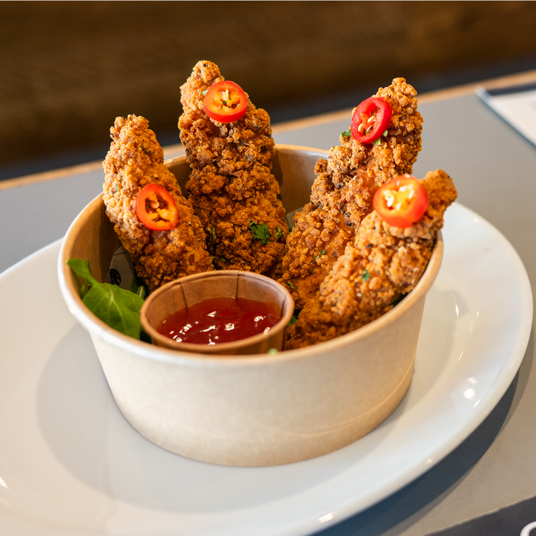 A bowl of fried chicken with red peppers and ketchup