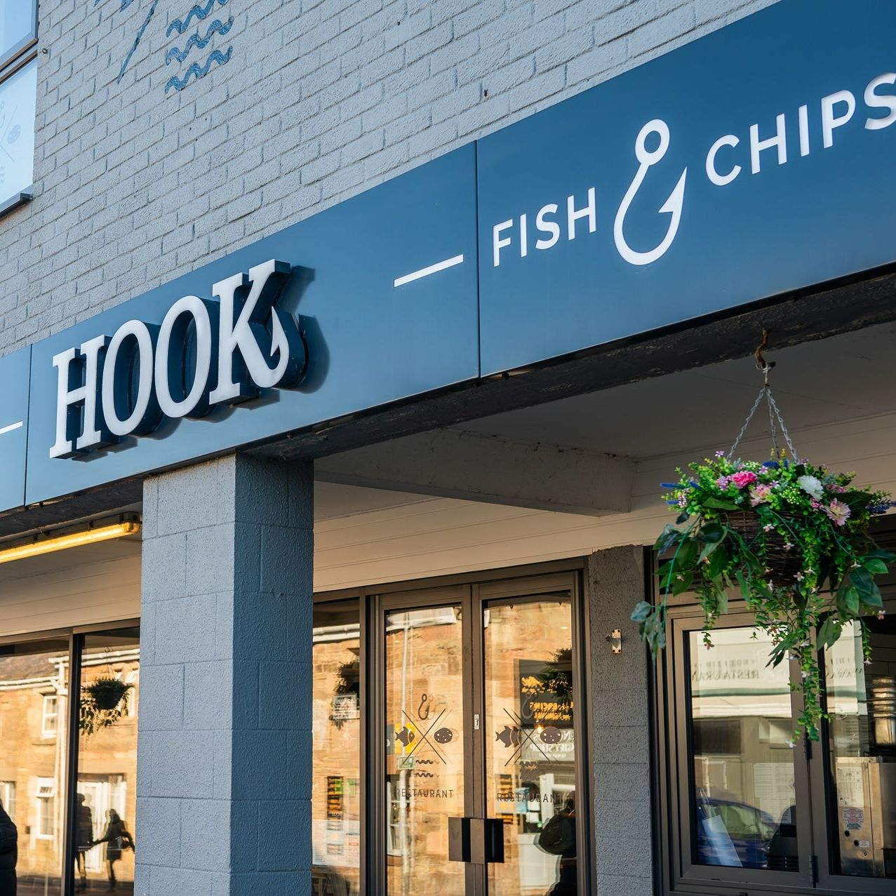 A hook fish and chips restaurant with a hanging basket of flowers