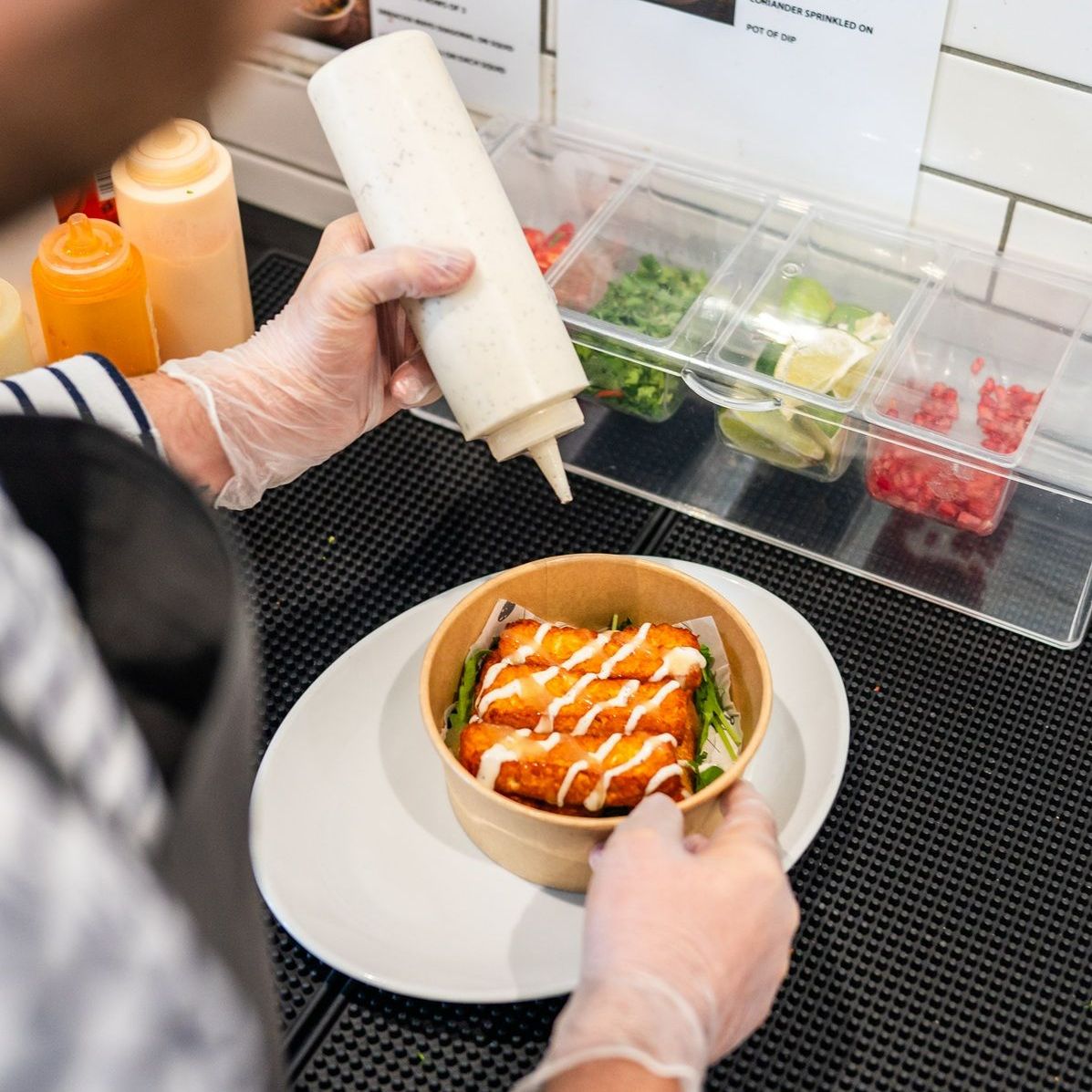 A person is pouring sauce into a bowl of food