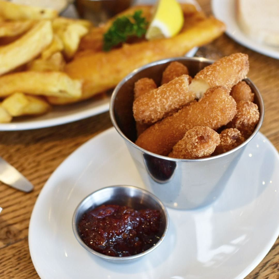 A bucket of mozzarella sticks sits on a plate next to a bowl of sauce
