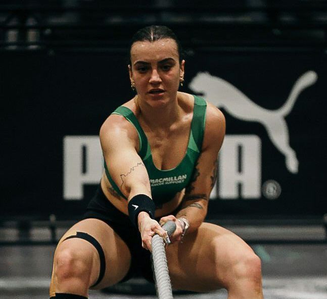 Woman in green sports bra and black shorts pulls a rope during a workout, Puma logo in the background.