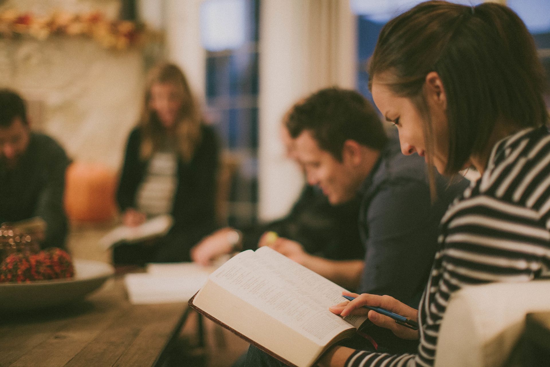 People seated indoors in a discussion group, one person reading from an open book
