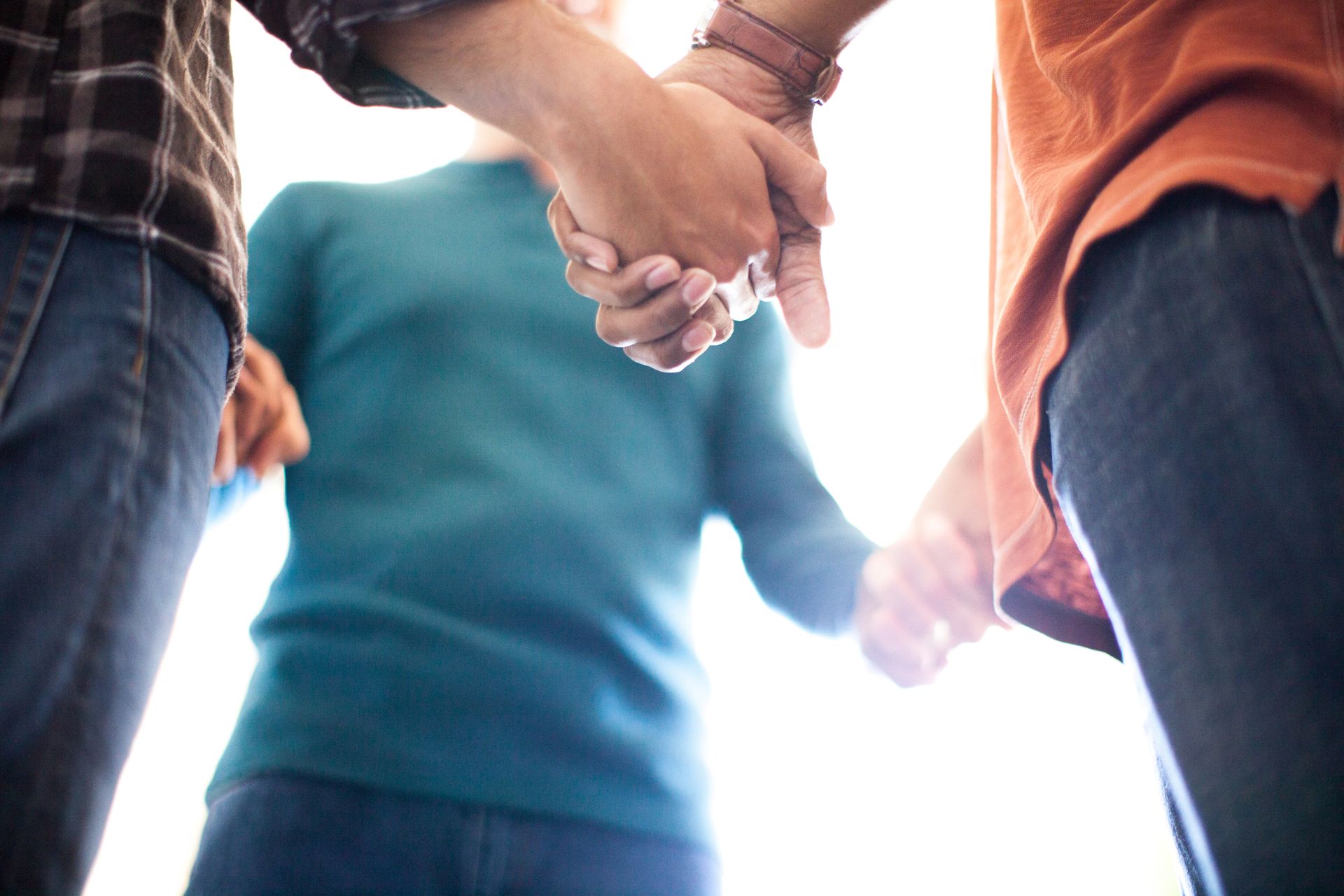 Three people holding hands in a bright outdoor circle