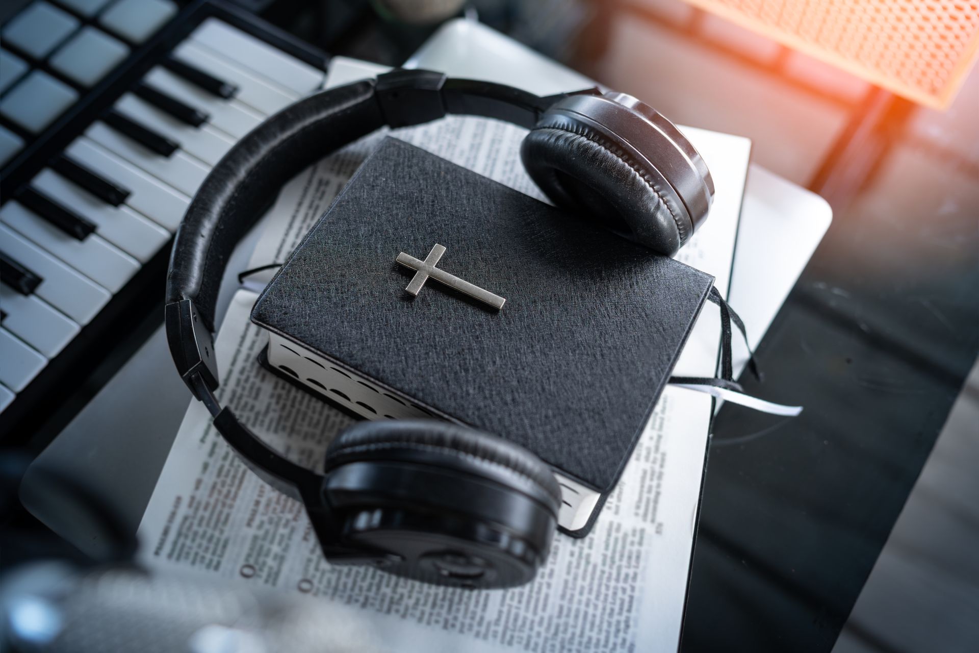 Headphones on a book with a cross, beside a piano keyboard and sheet music