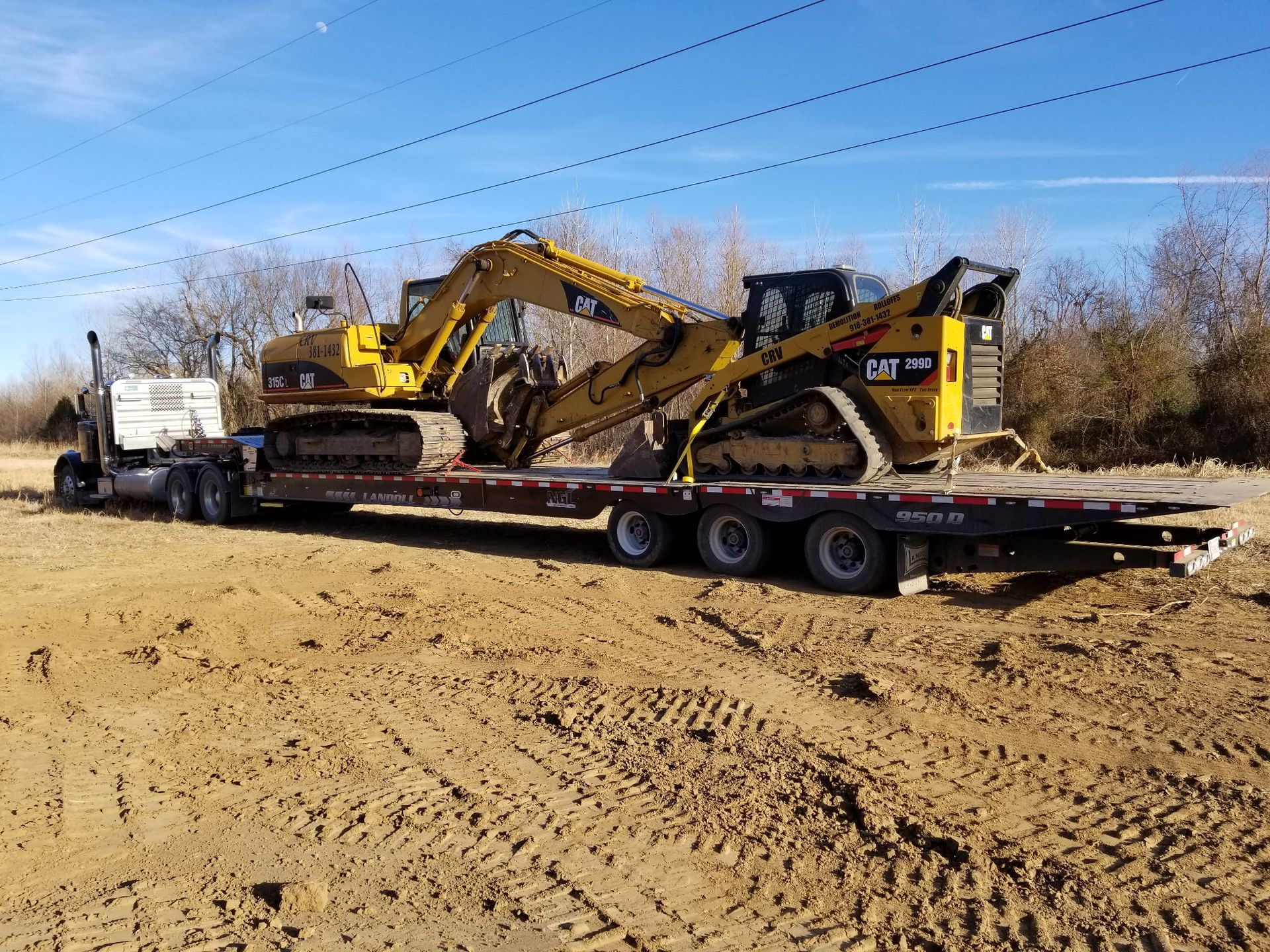 A flatbed trailer hitched to a truck carries a yellow Caterpillar excavator and a tracked skid steer on a dirt lot.