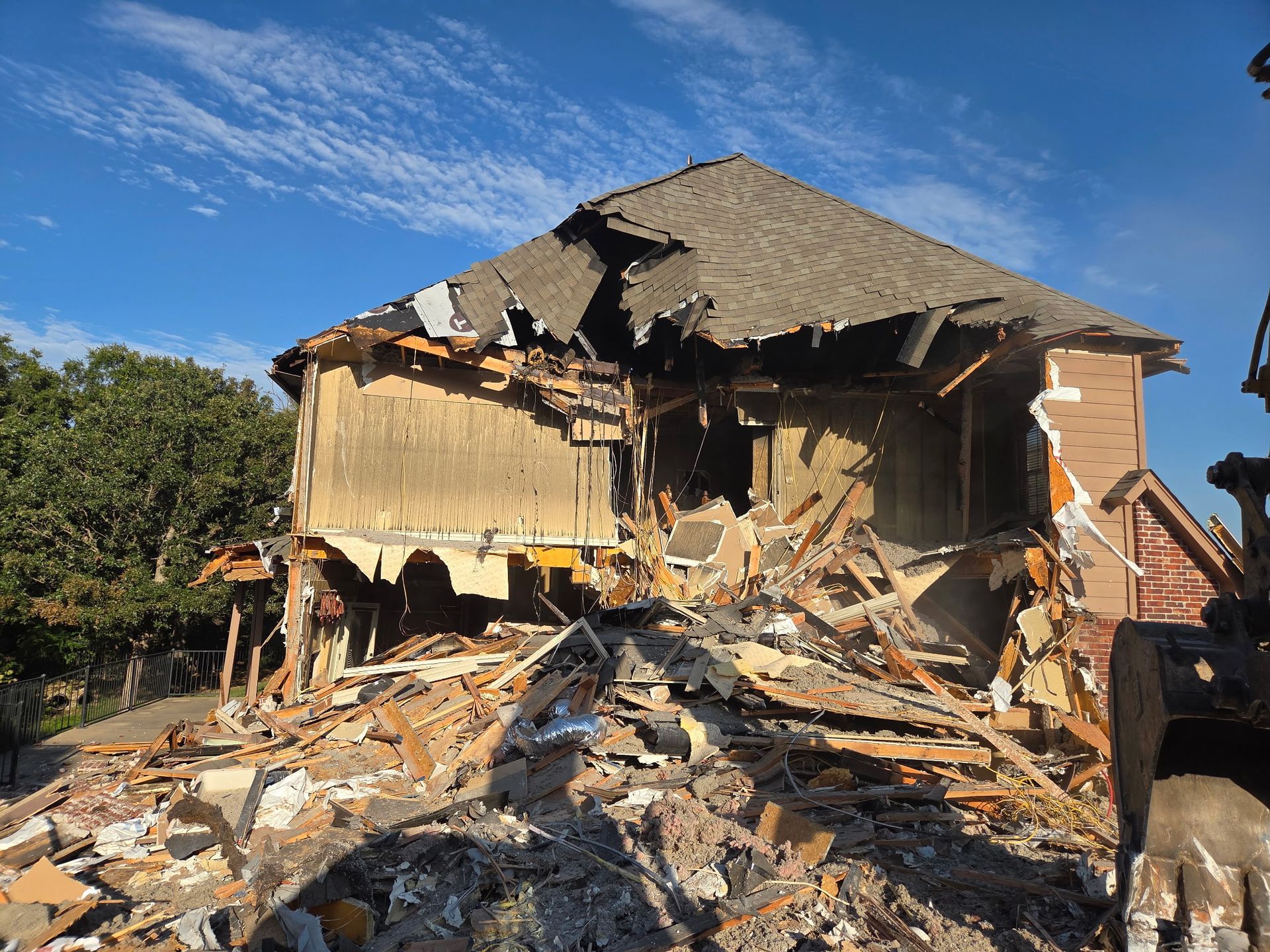 A partially demolished house with heavy debris in the foreground under a clear blue sky.