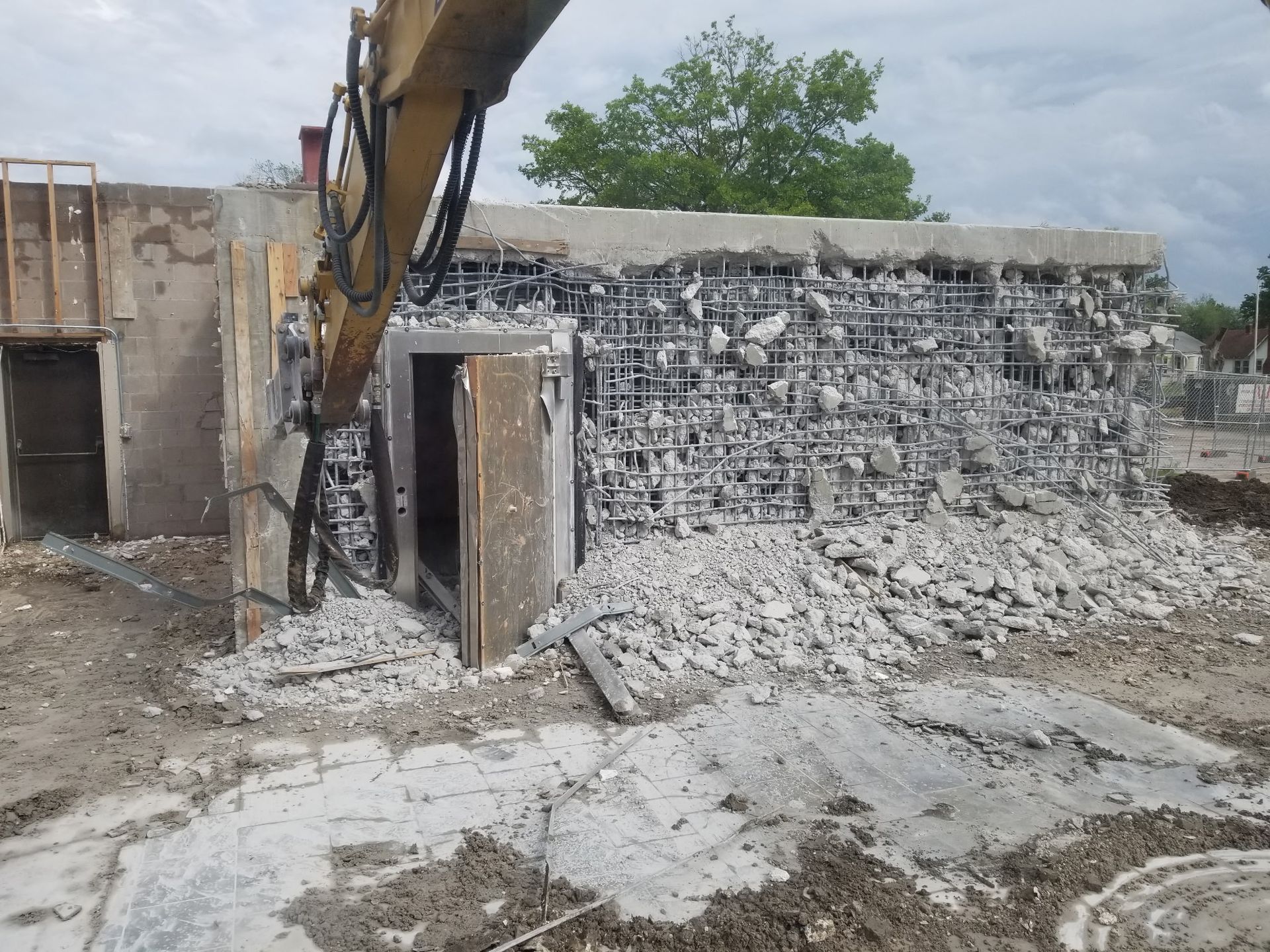 An excavator demolishes a concrete building, exposing the metal rebar structure inside.