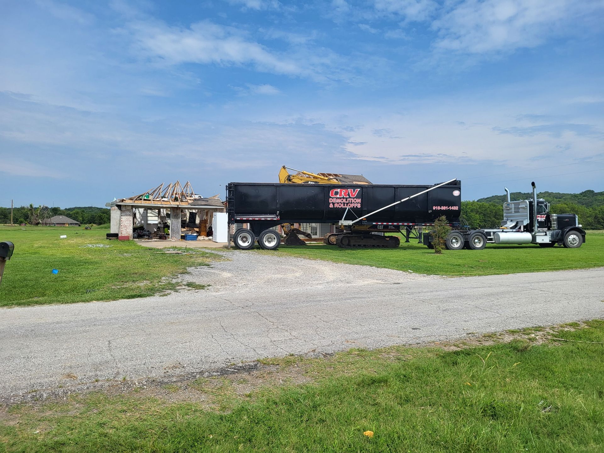 A black dump truck parked on a gravel driveway in a grassy field next to a partially demolished building.