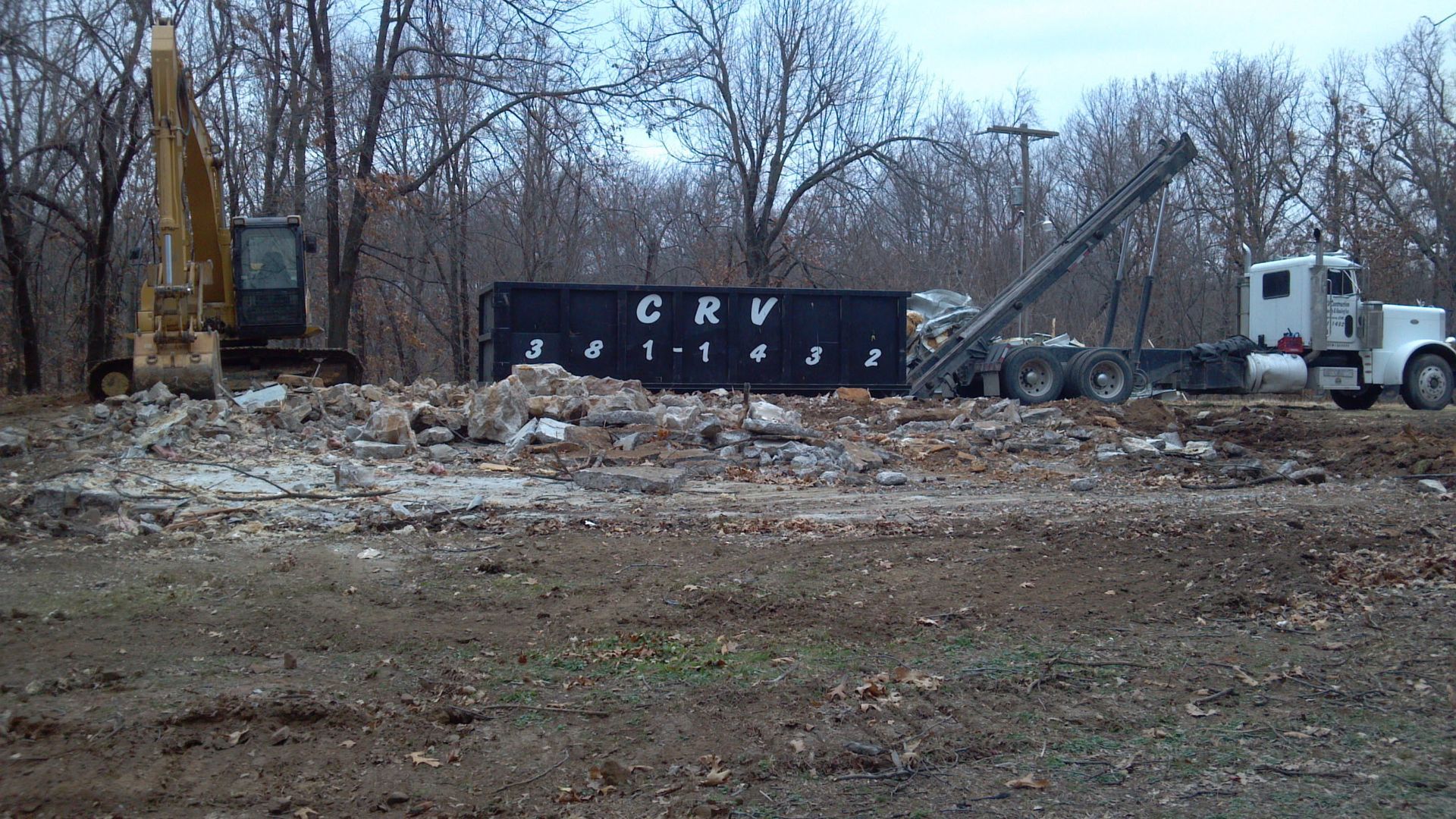 A construction site with an excavator, a large black debris dumpster labeled 