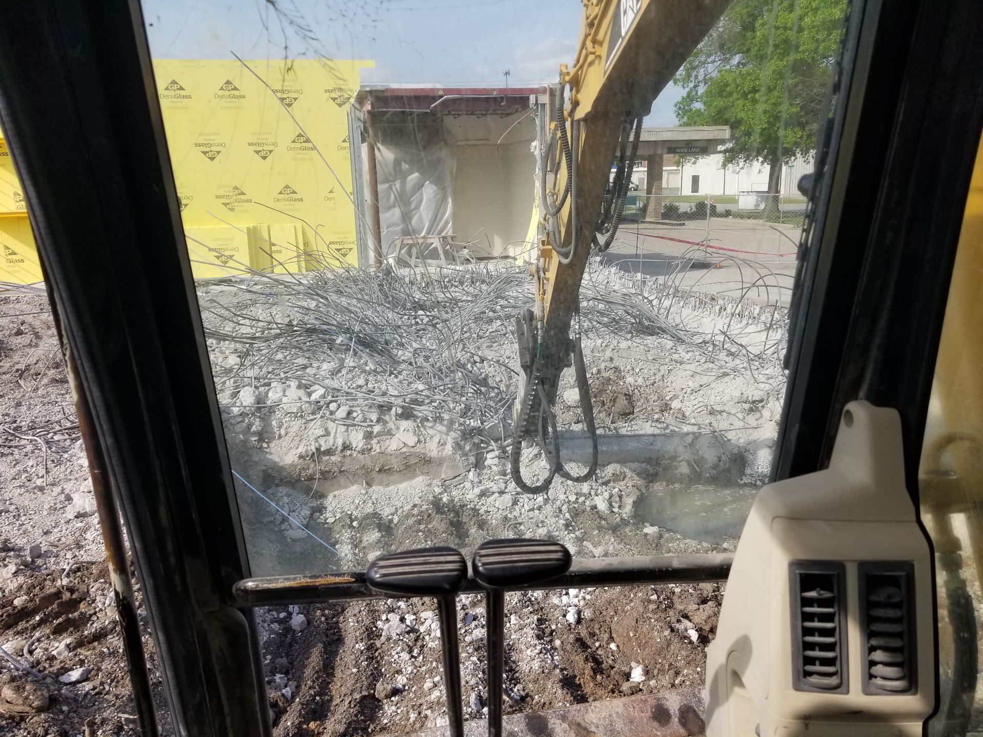 View from an excavator cab overlooking a demolition site with rubble and a partially demolished building.