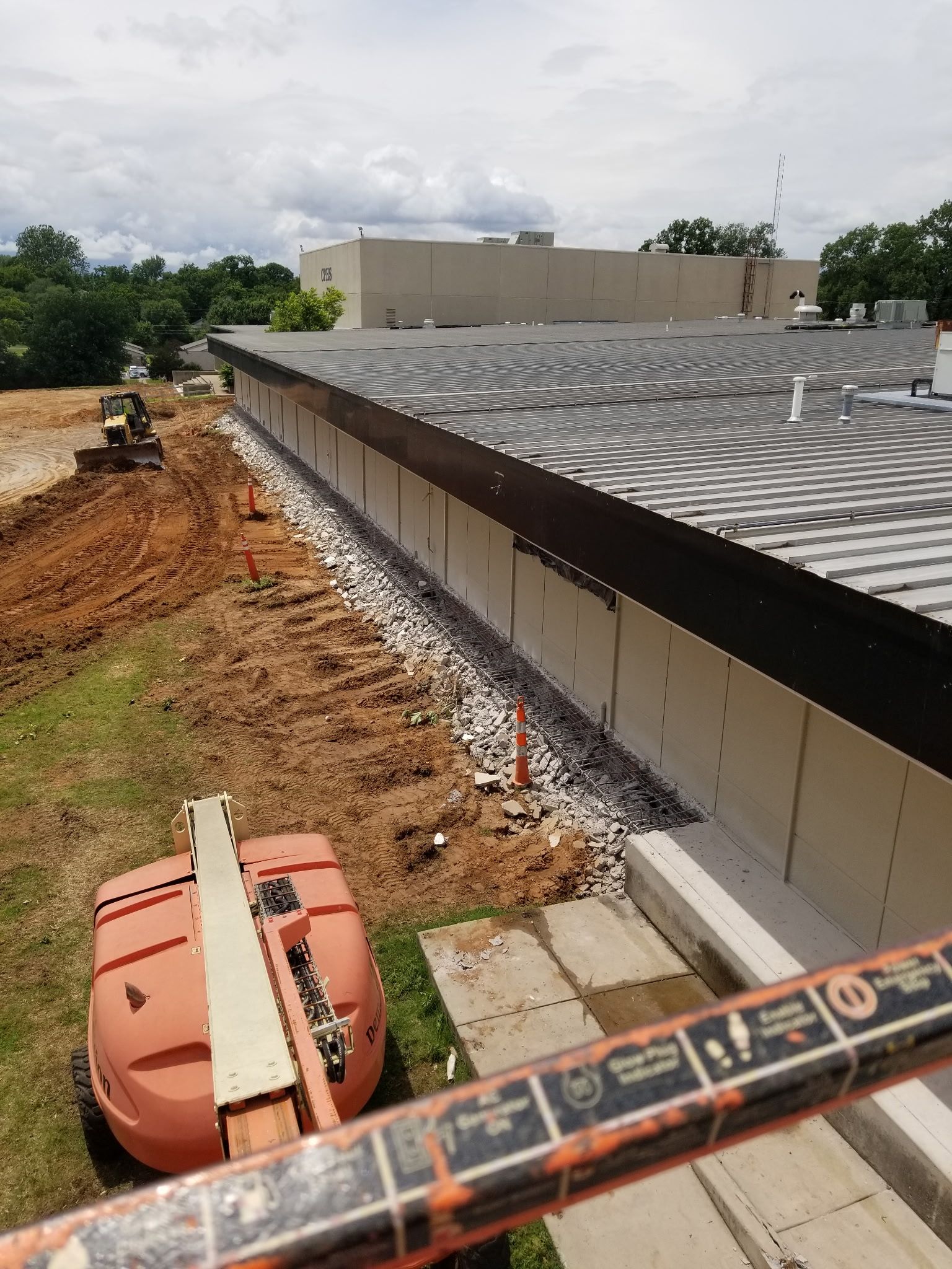 An elevated view of a construction site showing a large building exterior, piles of gravel, and heavy equipment.