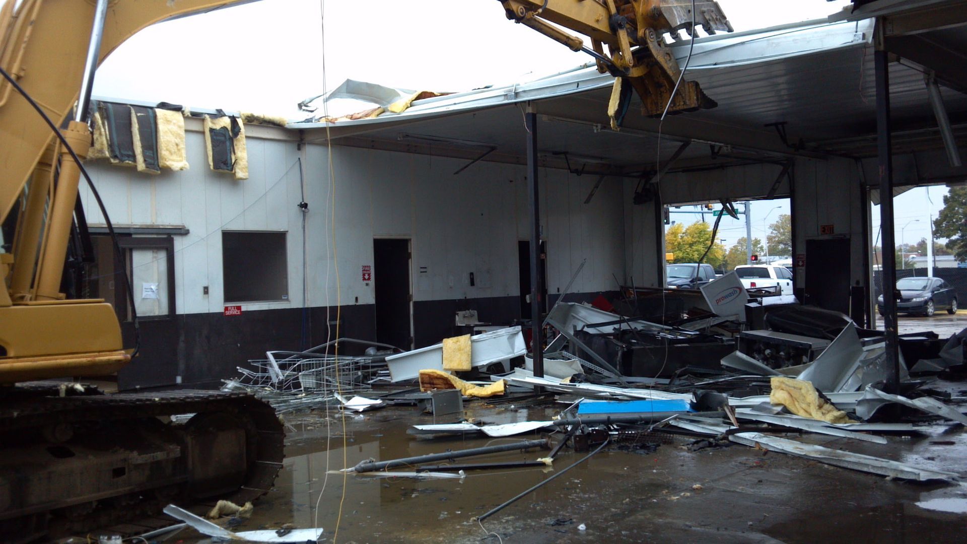 An excavator demolishes the interior of a damaged, debris-filled commercial building.