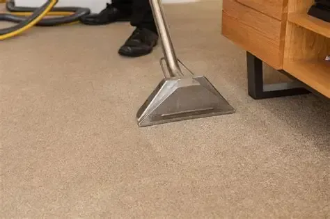 Carpet cleaning nozzle on beige carpet beside wooden furniture and a person’s shoe