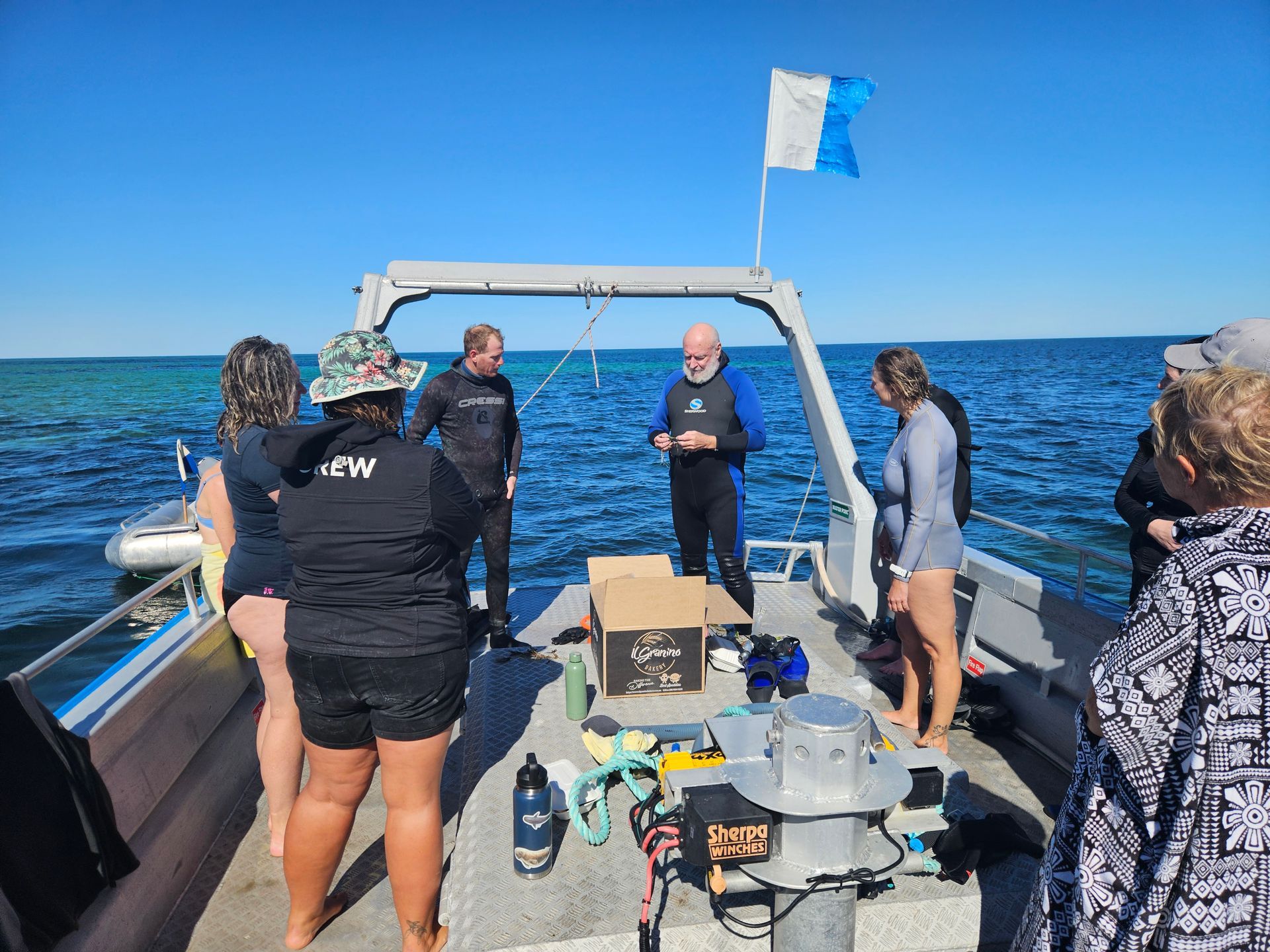 People on a boat, preparing to dive; clear blue water and sky; some wearing wetsuits.