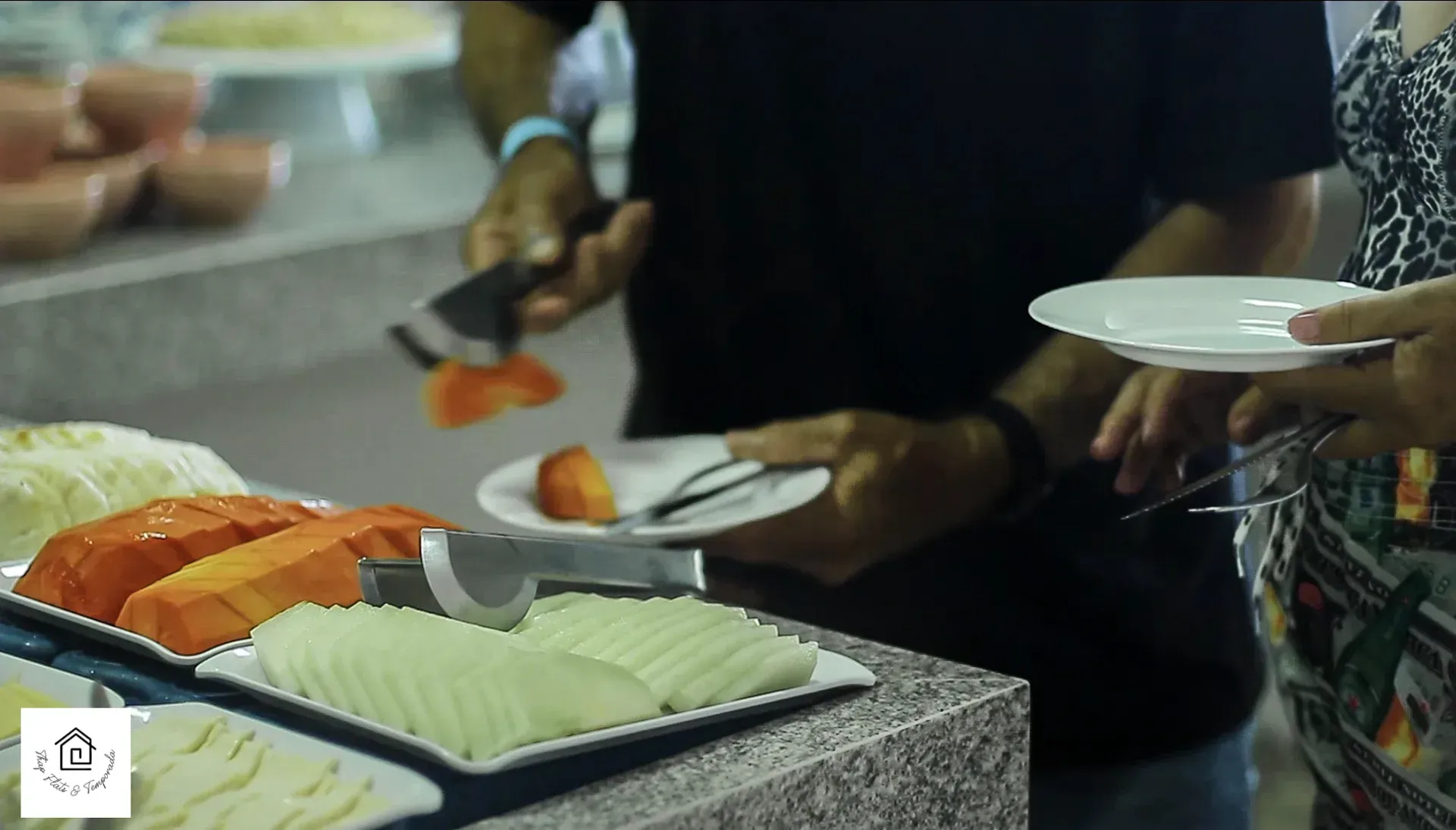 Um homem e uma mulher servem frutas em um buffet.